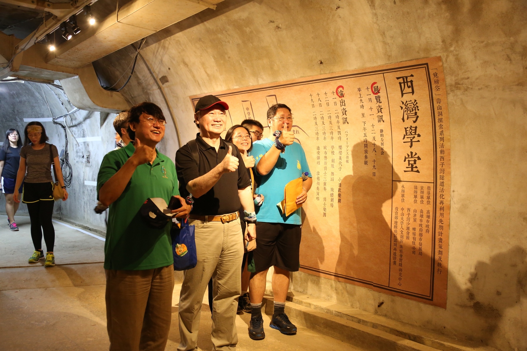 Visitors pose in front of exhibition poster.