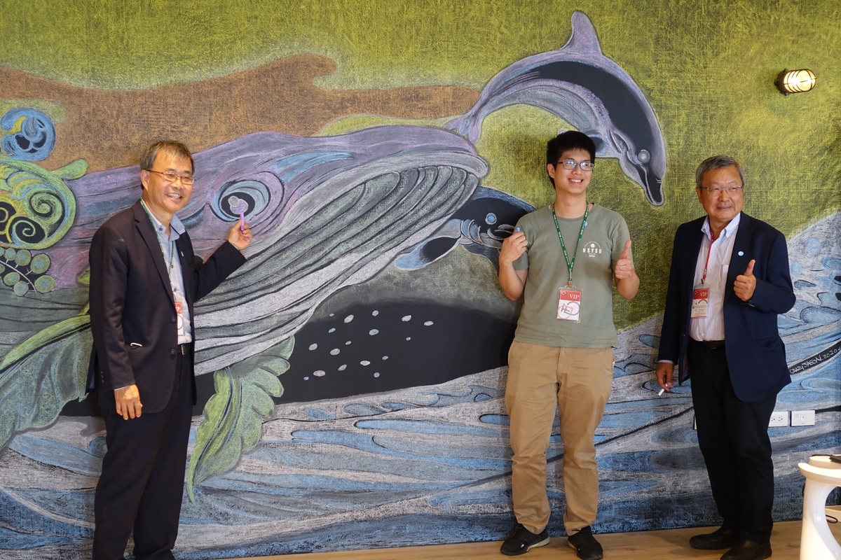 After a half-year’s construction, Si-Wan College Creativity Base is finally open. NSYSU President Ying-Yao Cheng (on the left), President of NSYSU Student Association Hao-Jun Chuang, and former Director-General of NSYSU Alumni Association and CEO of Lung Ching Steel Enterprise Owen Hsieh pose in front of a wall painting of dolphins and a whale in the Base.