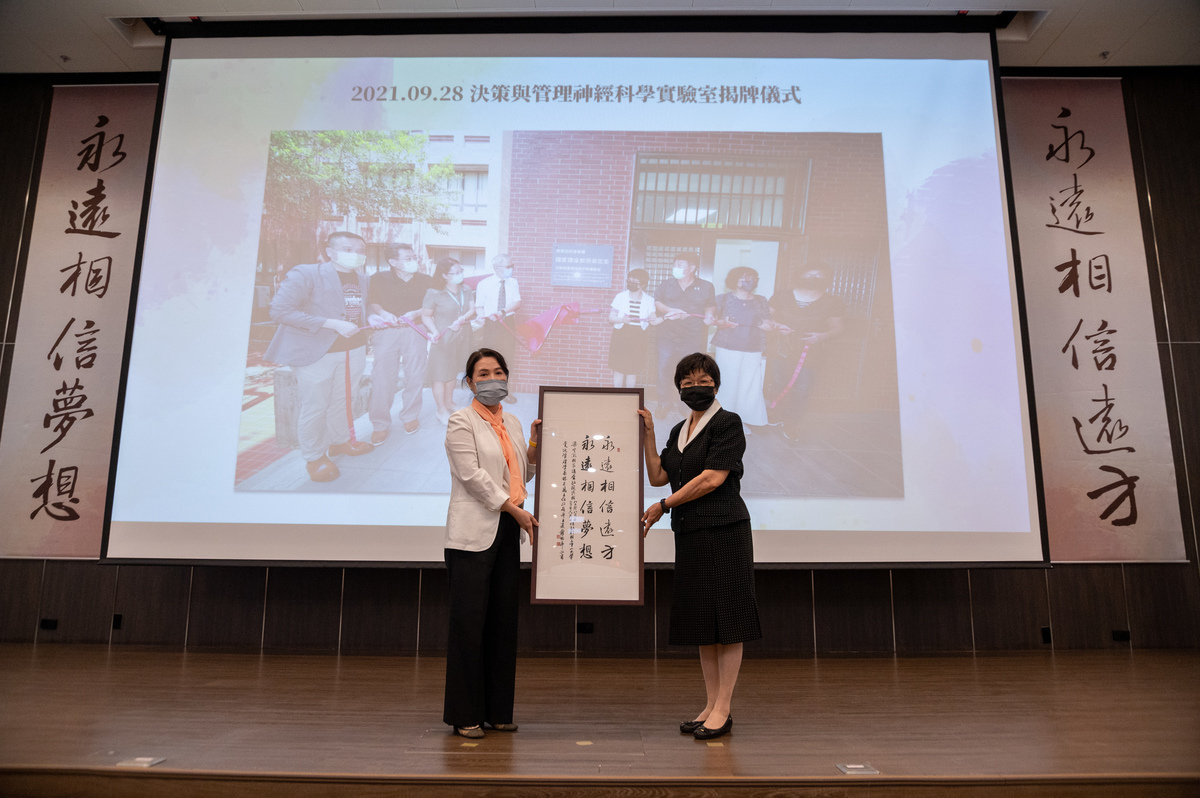 Chairperson of the Department of Information Management Fen-Hui Lin (on the left) hands calligraphy to Chen-Li Wang (on the right).