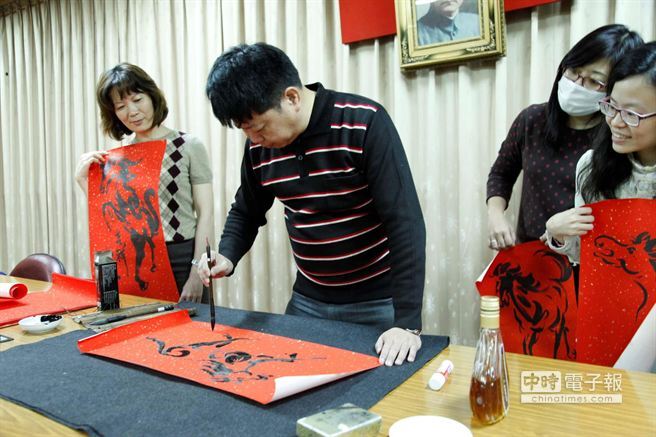 中山大學劇場藝術學系副教授王以亮（中）以酒墨揮毫畫春聯。（曹明正攝）圖片